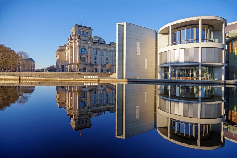 Modern and historic government buildings in Berlin, Germany, beautifully reflected in calm water during golden hour, with clear blue skies and warm sunlight