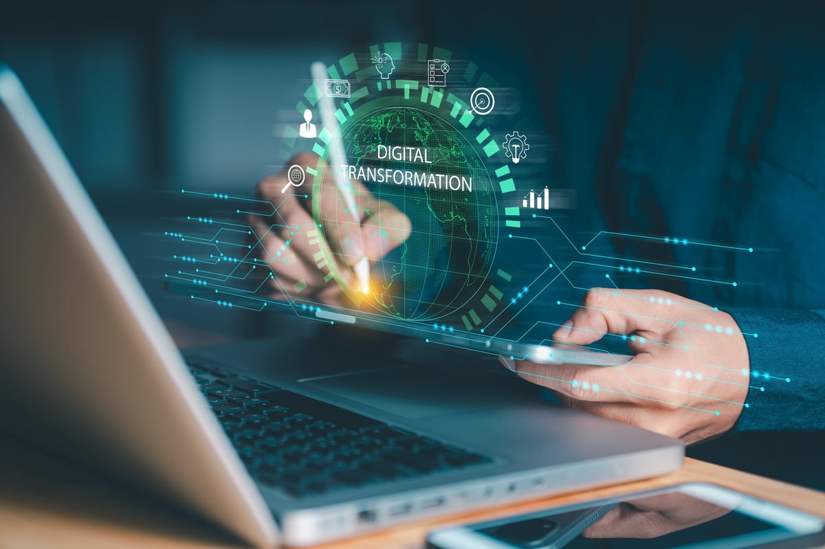 Person interacting with a tablet and laptop, featuring a glowing DIGITAL TRANSFORMATION sphere and business icons. Symbolizes applying technology for business evolution and data analysis