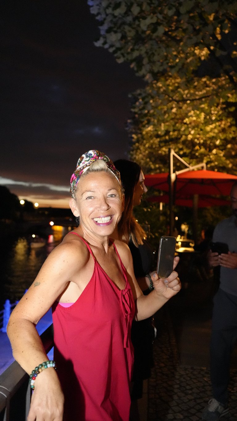 Woman in red halter dress with colorful headwrap smiling at evening outdoor event with illuminated trees