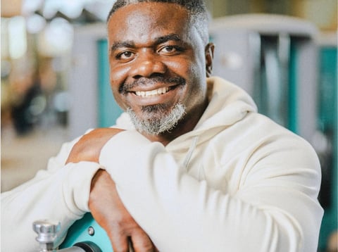 Portrait of a smiling man with gray hair and beard wearing a cream-colored hoodie in an indoor setting